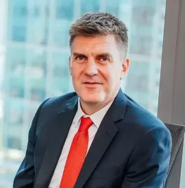 Person in a suit with red tie, sitting by a window in an office.
