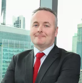 Person in a suit with a red tie smiling, city skyline in background.