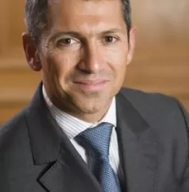 Person in a suit with a neutral expression and wooden background.