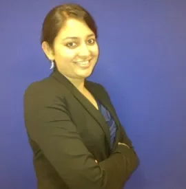 Person in a black blazer smiling in front of a blue background.