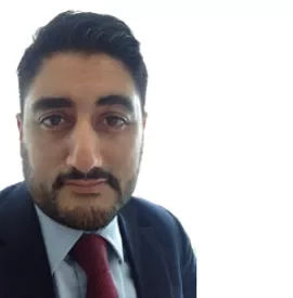 Person in a suit with a red tie, facing the camera against a bright background.