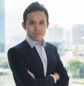 Person in a suit standing with arms crossed in front of a cityscape background.