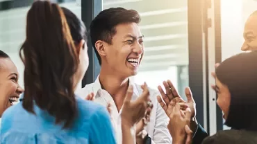 A group of people laughing and clapping in an office setting.