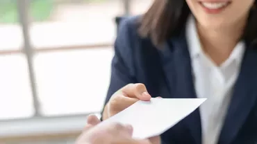 Person in a suit handing a white envelope to another individual.