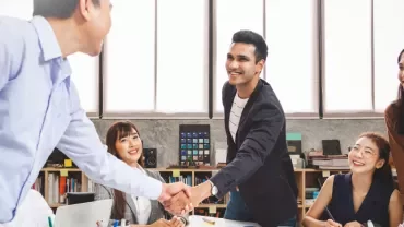 Group of people in an office smiling and shaking hands.