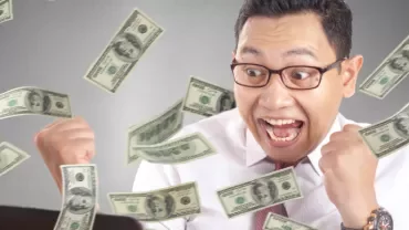 Excited person with glasses surrounded by falling dollar bills.
