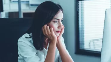 Person sitting at desk, looking at computer screen in bright office.