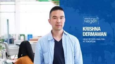 Person standing in an office environment with people working in the background.