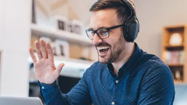 Person wearing headphones, smiling and waving at a laptop.