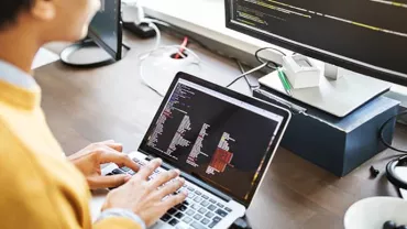 Person coding on a laptop with a monitor displaying code