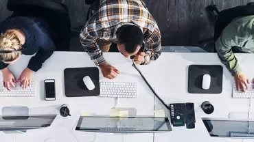 Three people working at computers in a modern office space.