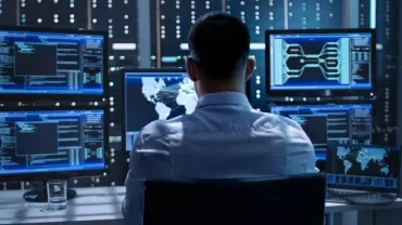 Person working at a desk with multiple computer monitors displaying data and a world map.