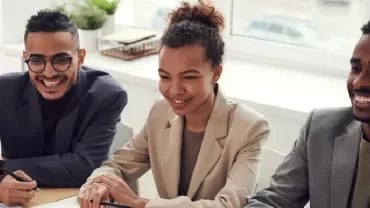 Three people sitting at a table, smiling during a meeting.