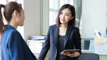 Two people in formal attire having a conversation in an office.