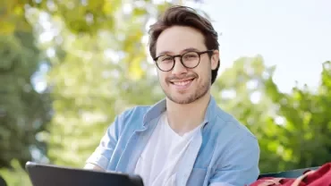 Person smiling outdoors sitting on a bench with a tablet.