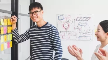 Person smiles while presenting colorful sticky notes on a board.