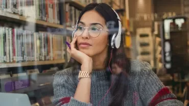 Person wearing headphones sitting in a library, looking thoughtful.