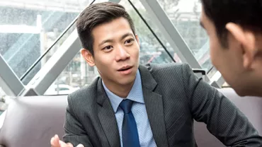 Two people in business attire are engaged in a conversation in an office setting.