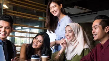 Group of people smiling and discussing around a laptop in a modern office.