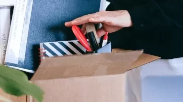 Person packing books and office supplies into a cardboard box.