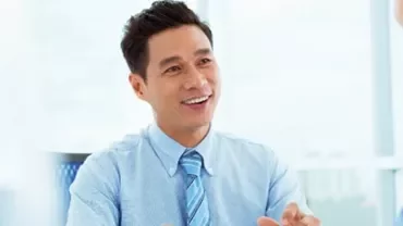 Person in a blue shirt smiling and talking to someone in a light office.