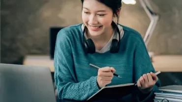 Person with headphones studying on a laptop at a cozy desk.