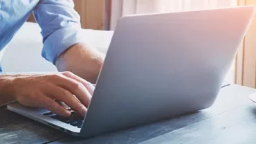 Person typing on a laptop at a wooden table with a cup of coffee beside them.