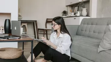 Person sitting on floor in living room, working on a laptop and taking notes.