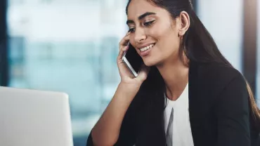 Person smiling while talking on the phone and working on a laptop.