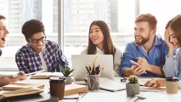 Group of people laughing and studying together at a table.