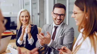 Group of professionals in a meeting, smiling and clapping.