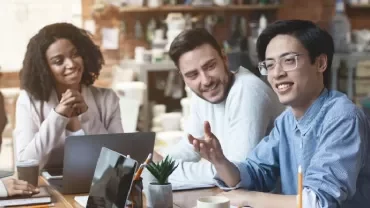 Group of people having a meeting around a table with laptops and notebooks.