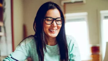 East Asian female professional smiling as she works on the laptop.