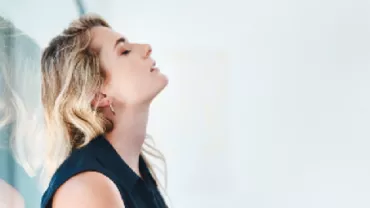 Person leaning against a reflective window with eyes closed.