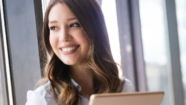 Person smiling while looking out a window with a laptop.