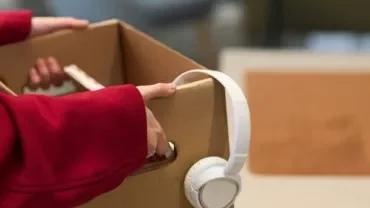 A person holding a box containing a pair of headphones.