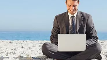 Person in a suit sitting on a beach with a laptop.