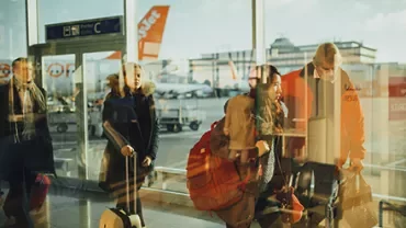 Travelers with luggage walk through a bright airport terminal.