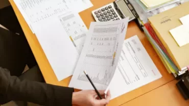 Person holding financial spreadsheets at a desk with a calculator.