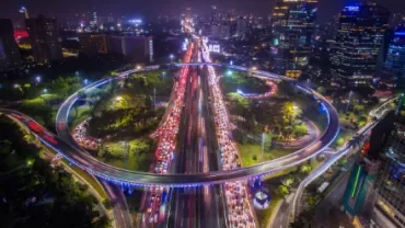 Aerial view of a busy city highway interchange with vibrant lights at night.