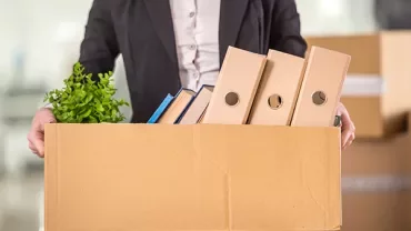 Person holding a cardboard box with files and a plant.