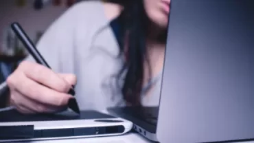 Person using a digital pen and tablet in front of a laptop.