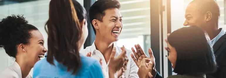 A group of people laughing and clapping in an office setting.