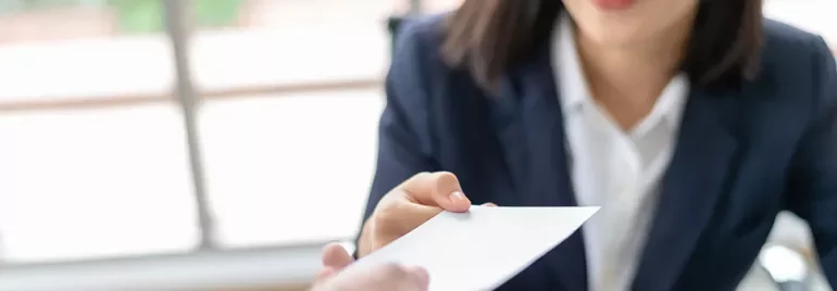 Person in a suit handing a white envelope to another individual.