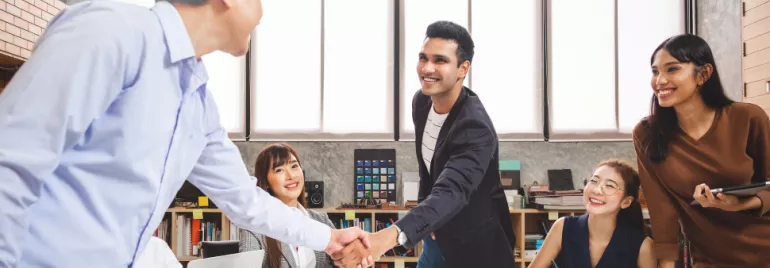 Group of people in an office smiling and shaking hands.