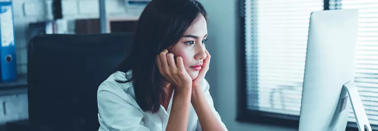 Person sitting at desk, looking at computer screen in bright office.