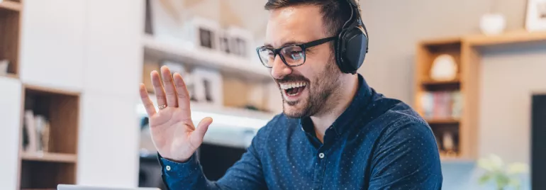 Person wearing headphones, smiling and waving at a laptop.