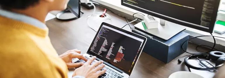 Person coding on a laptop with a monitor displaying code