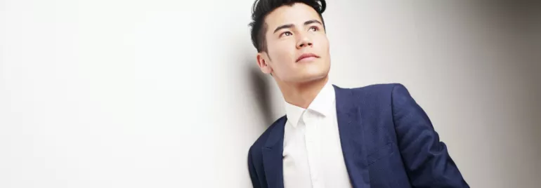 Person in a blue suit and white shirt gazing upwards against a light background.