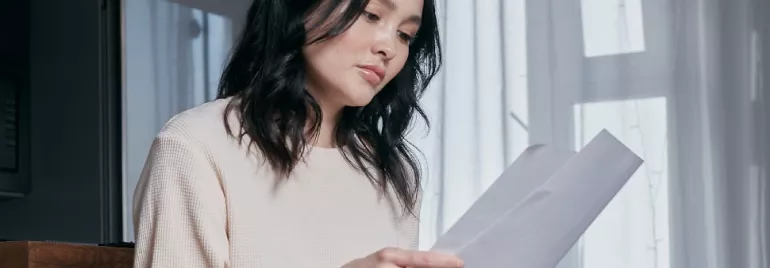 Person seated, holding and reading papers by a window.